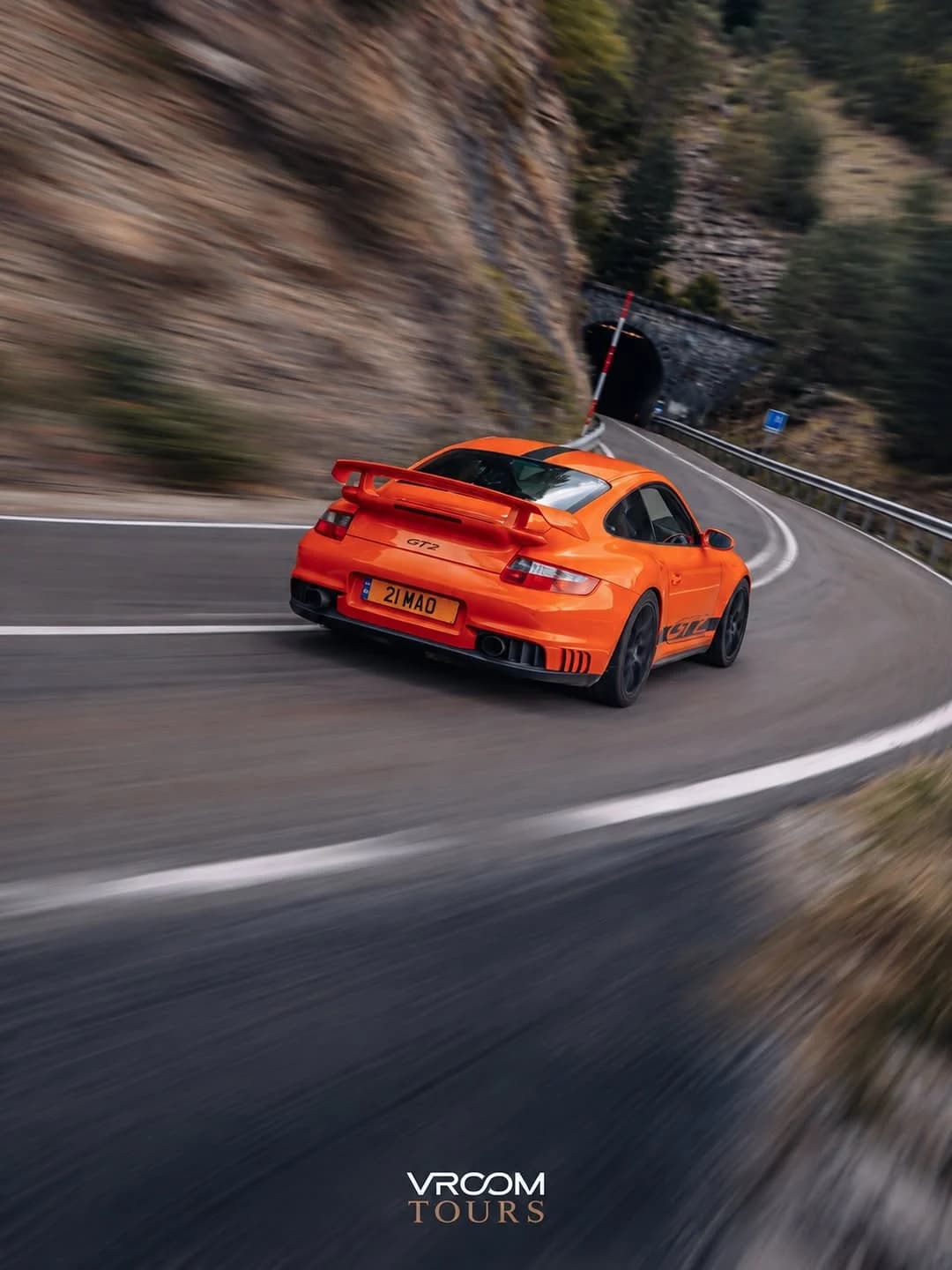 An orange Porsche following a mountain road towards a tunnel