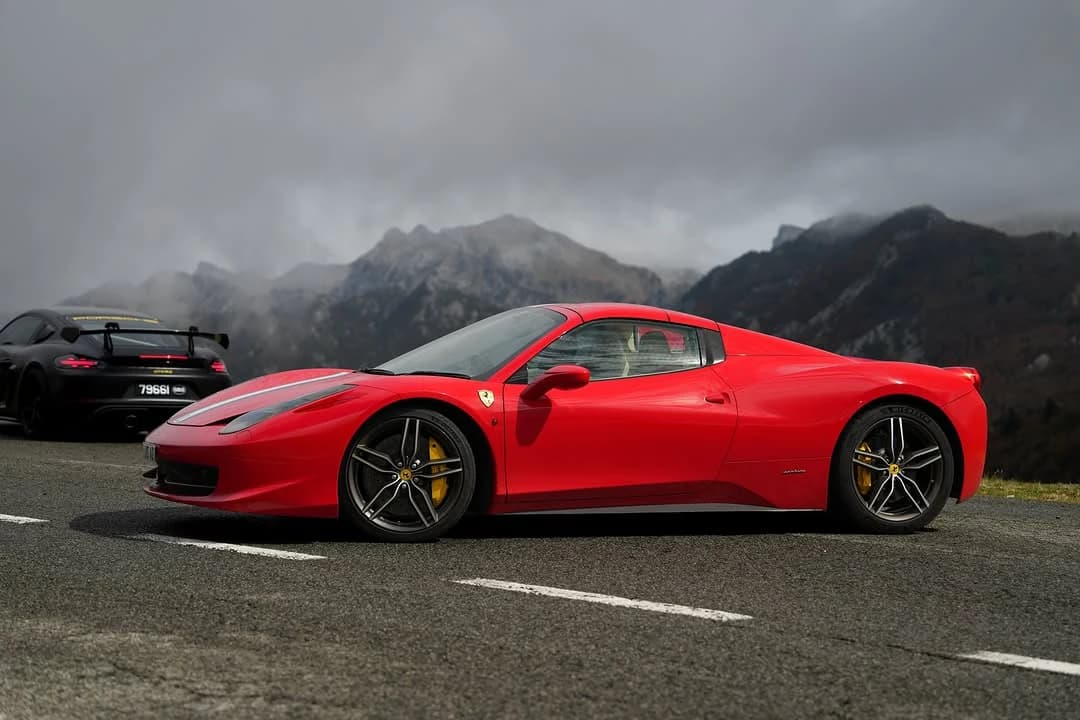 A red Ferrari and black Porsche beneath misty Pyrenees mountains